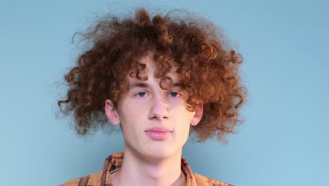 a guy with curly hair is looking at the camera on a blue background in the studio a guy with curly hair is looking at the camera on a blue background in the studio
