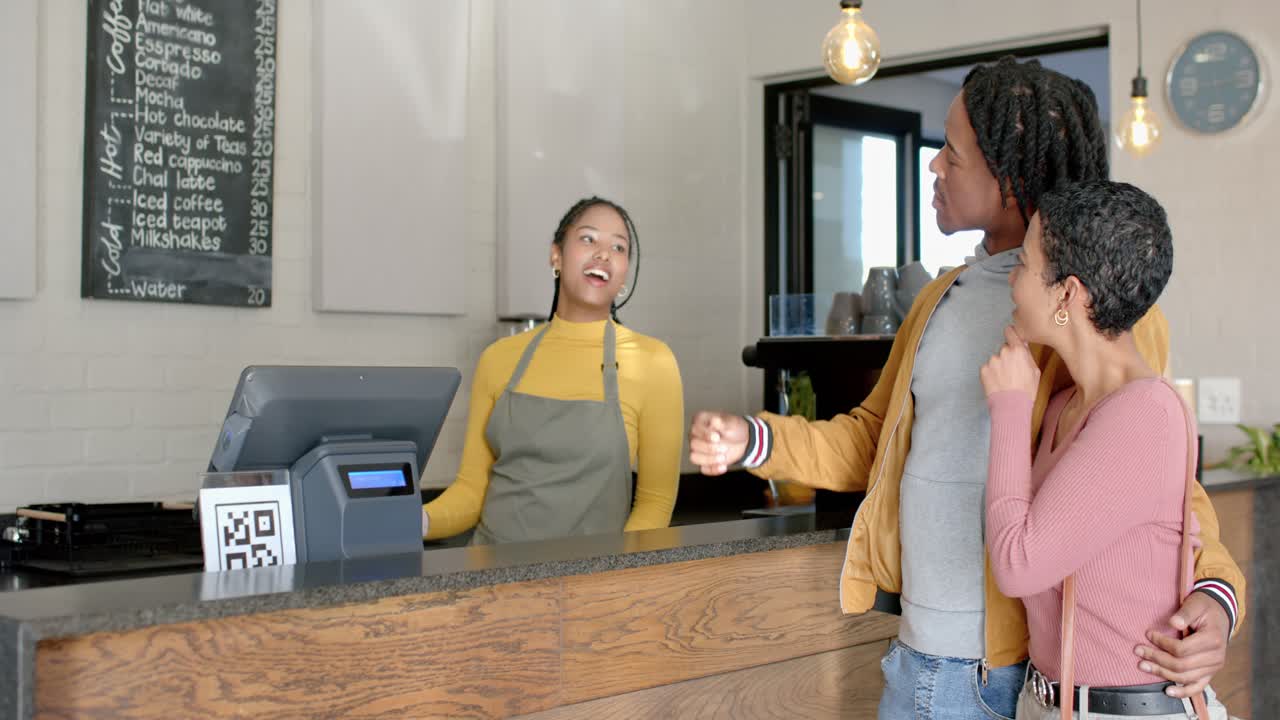 Diverse couple approaching cafe counter greeting apron barista pointing menu and ordering coffee