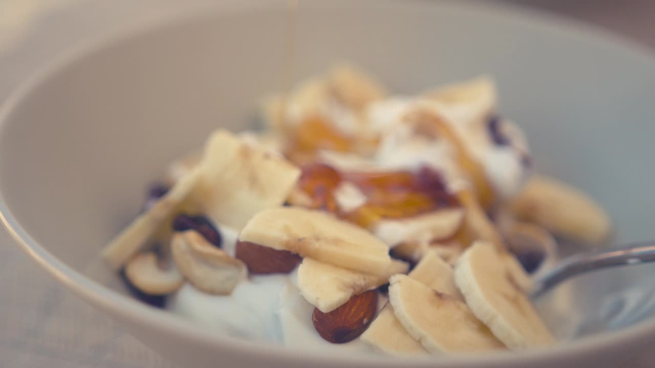 Miele versato a filo su una ciotola di yogurt greco, noci e banane