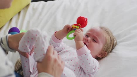 caucasian mother playing with her baby holding a toy in the bed at home