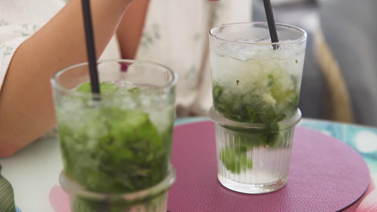 primer plano de una mano arremolinándose cubos congelados en un vaso de agua con menta
