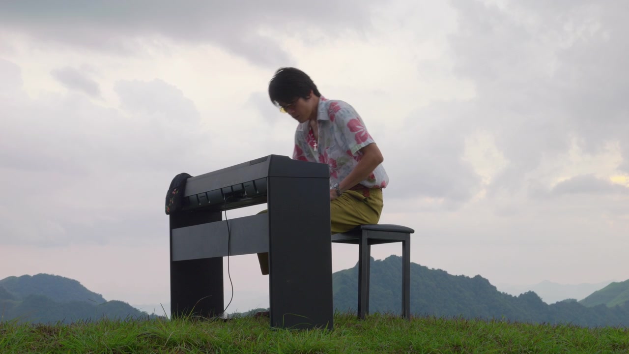 Pianista Asiático Caminha até o Piano e Prepara-se para Tocar em Colina de Montanha ao Pôr do Sol. Inspiração Musical Criativa na Natureza Tropical.