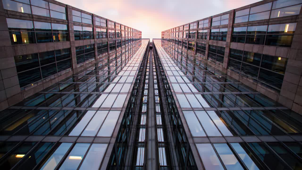 Views directed upwards reveal a striking structure of glass and steel in an urban area. The building's design emphasizes symmetry and light, creating a captivating visual experience.
