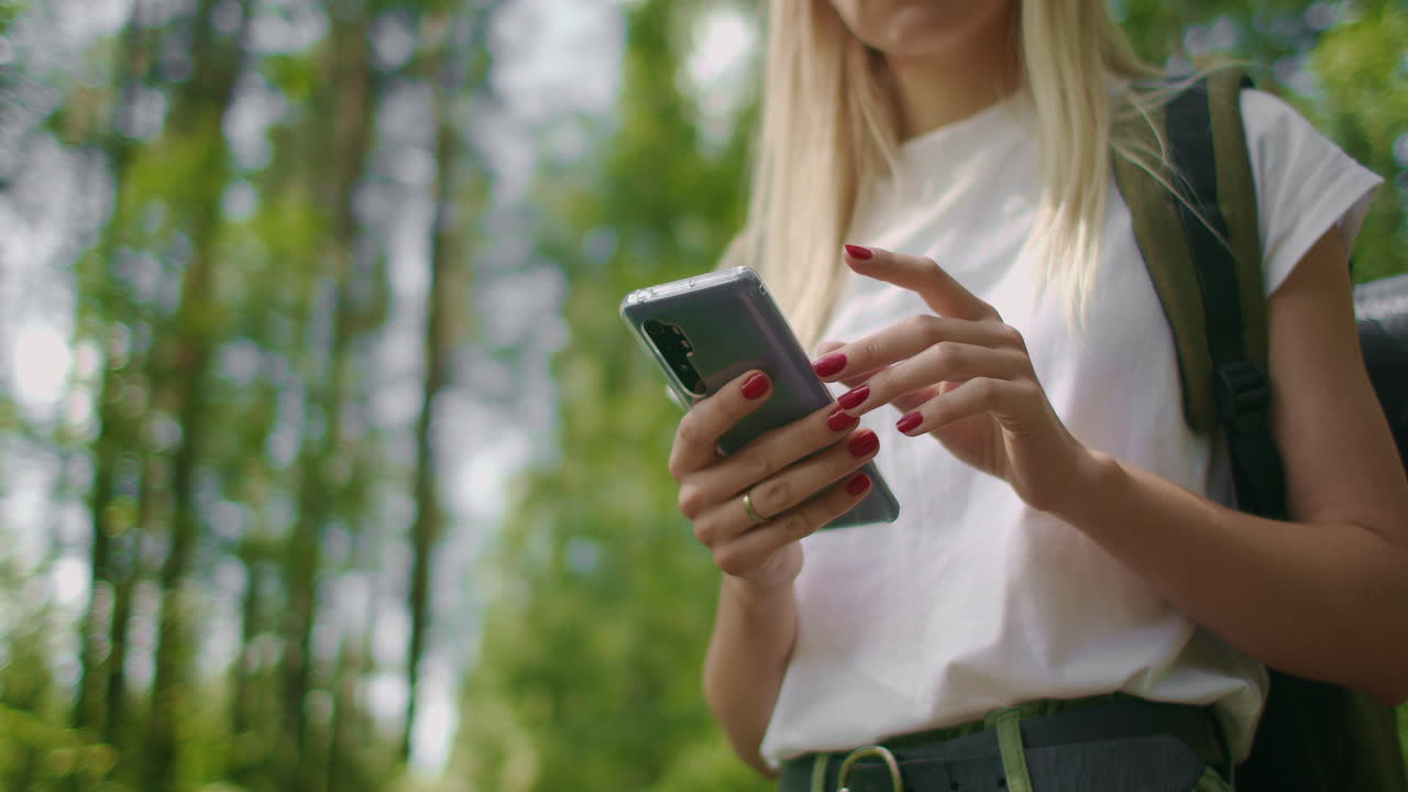 Close-up of a mobile phone in the hands of a female traveler walking through the forest. Social networks Navigator and messenger. Use your mobile phone for a walk in the woods