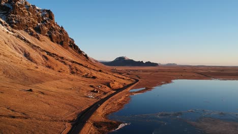 majestic drone shot a car driving on isolated road in south coast of iceland through a landscape bathed in golden light, next to a ice lake with stunning blue water reflecting the azure of the sky