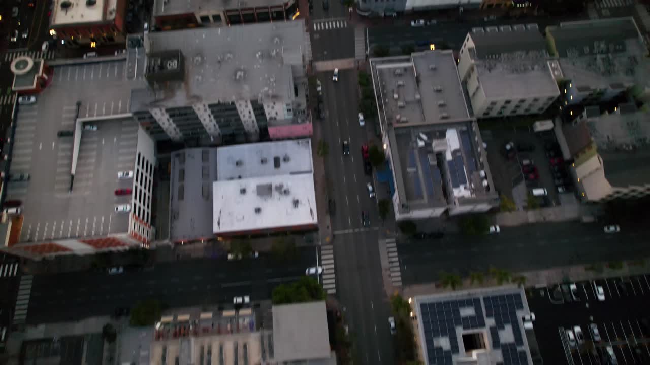 Segunda tomada de drone voando para trás ao pôr do sol com a câmera inclinando para baixo sobre os edifícios do centro de San Diego.