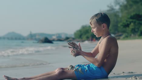 joyful-boy-sits-and-throws-wet-sand-on-pictorial-ocean-beach