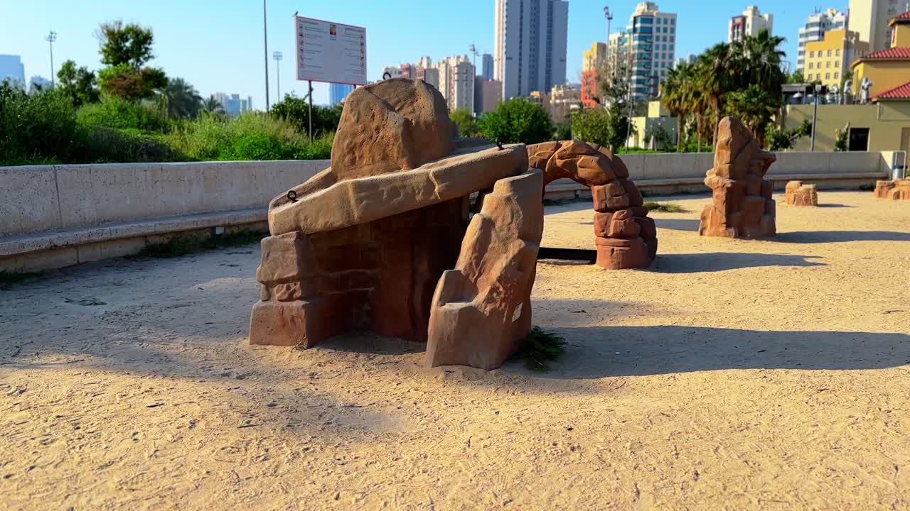A scenic 4K shot of a unique stone sculpture in a sandy urban park with city skyscrapers in the background. Ideal for themes of architecture, nature, and urban planning.
