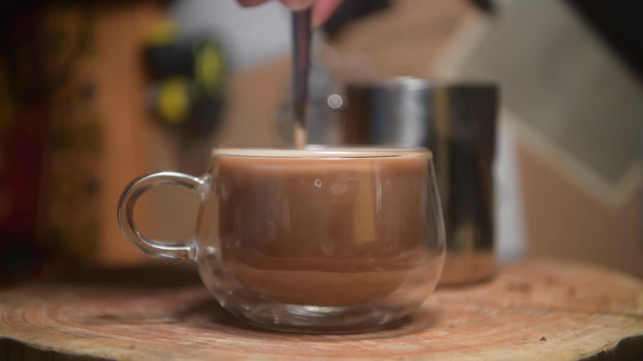 Tazza di vetro di tè o caffè su un tagliere di legno rustico che viene mescolato.