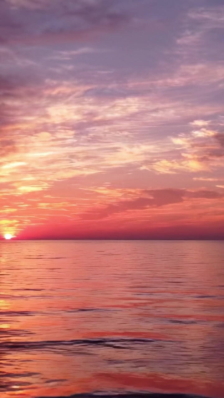 A Stunning Sunset by the Water: A Colorful Display of Vibrant Hues Reflecting on Calm Ocean Waves as the Sun Sinks Below the Horizon