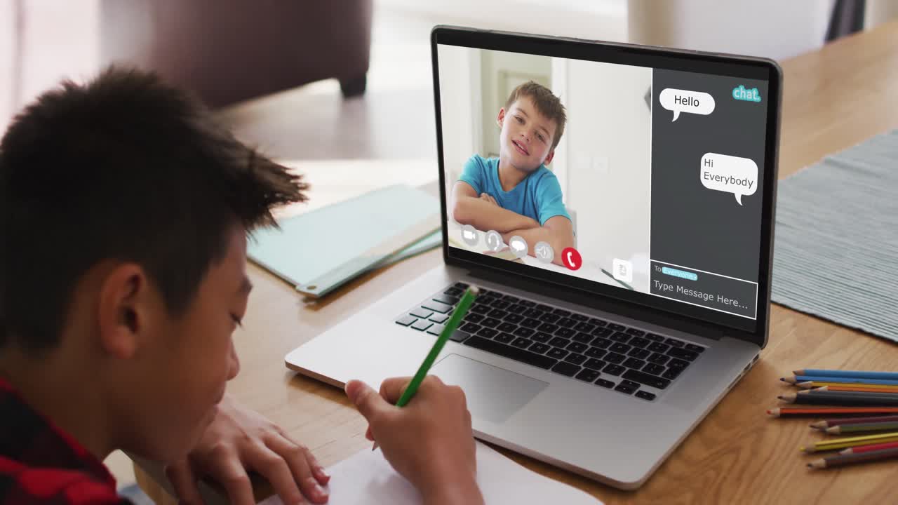 Schoolboy using laptop for online lesson at home, with school friend and web chat on screen