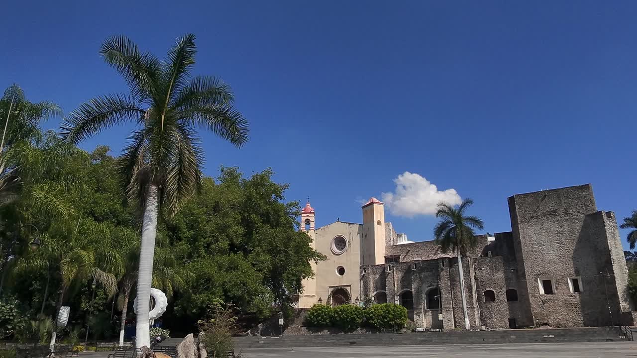 Old convent facade in Tlayacapan, Mexico, with palm trees and clear blue sky