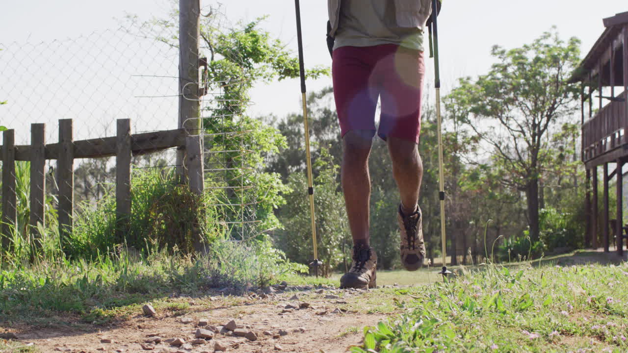 Senior african american man hiking with trekking poles on sunny day, slow motion