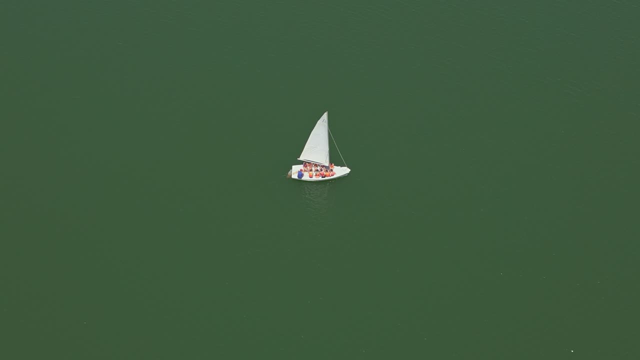 Sailboat sailing on green water on sunny day. Crew and passengers on board ship. Aerial view. Andalusia. Spain.
