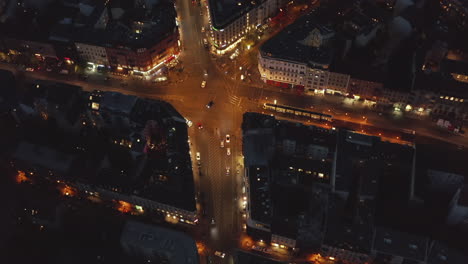 Aerial-Birds-Eye-View-over-Berlin,-Germany-Neighborhood,-intersection-at-night-with-glowing-street-traffic-city-lights-at-Rosenthaler-Platz,-Top-View-of-Cityscape-at-Night