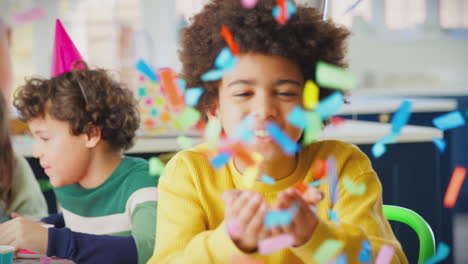 boy blowing confetti at camera at birthday party with friends and parents at home