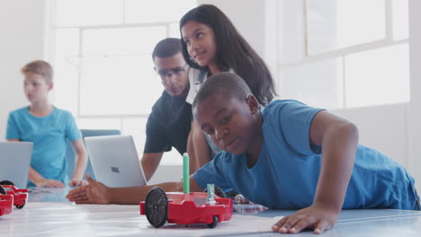 estudiantes con un maestro masculino en una clase de codificación de computadoras después de la escuela aprendiendo a programar un vehículo robot