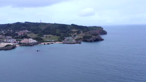 Aerial-view-of-Cantabria-coastline,-Isla-town-with-touristic-resorts-by-turquoise-colored-water,-Spain