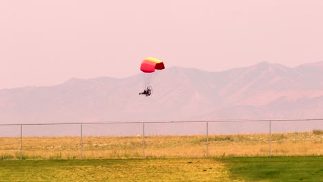 un parapente motorizado cruzando el cielo al atardecer con las montañas al fondo