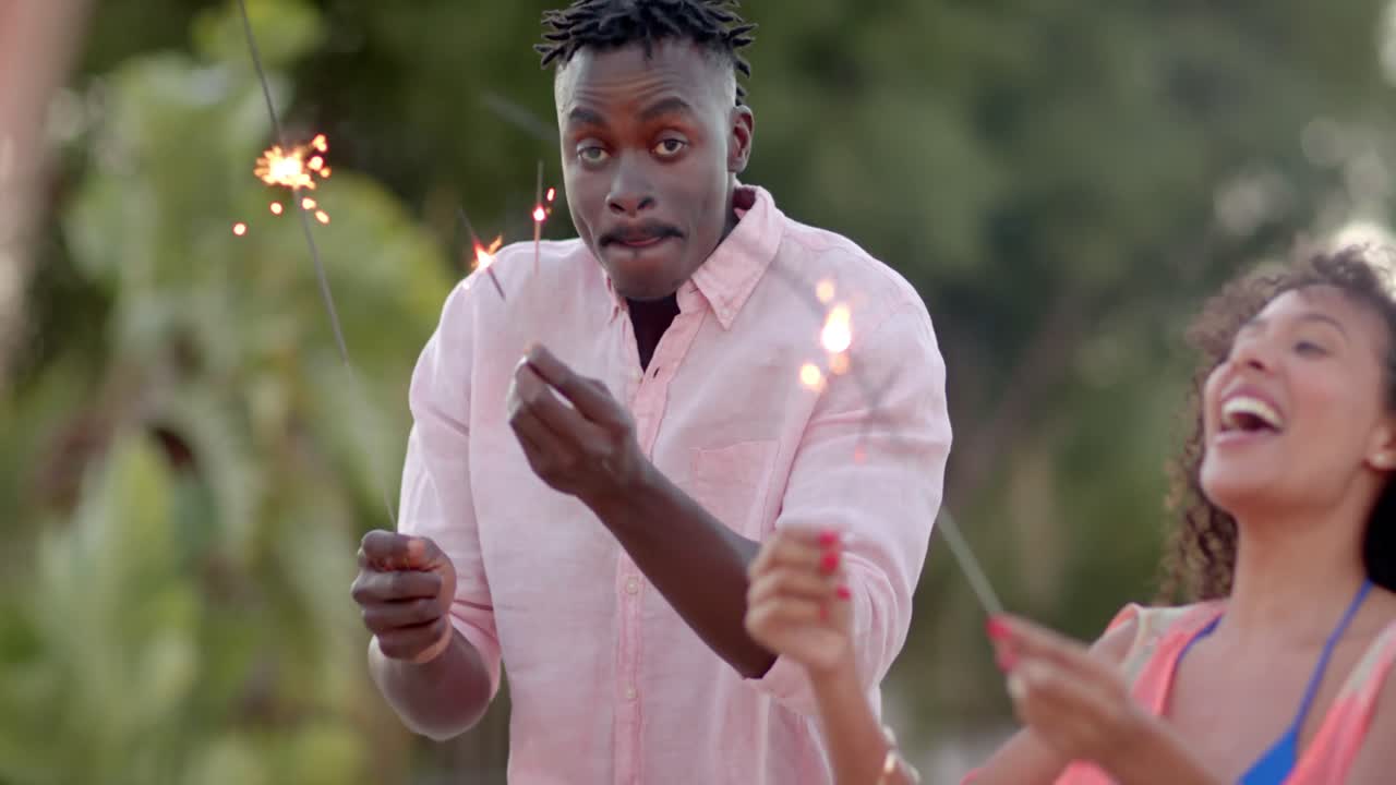 해변에서 반 ⁇ 이는 불꽃과 함께 춤추는 다양한 친구들의 행복한 그룹