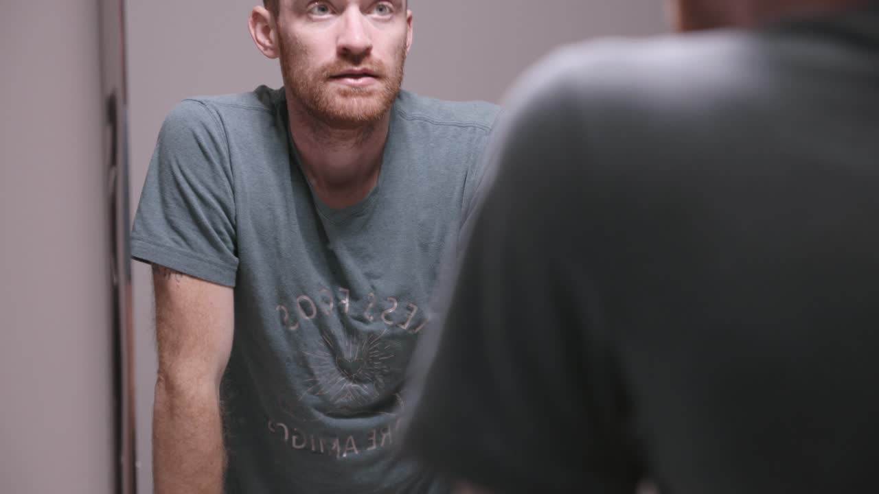 Man in bathroom looking in the mirror and splashing water on his face