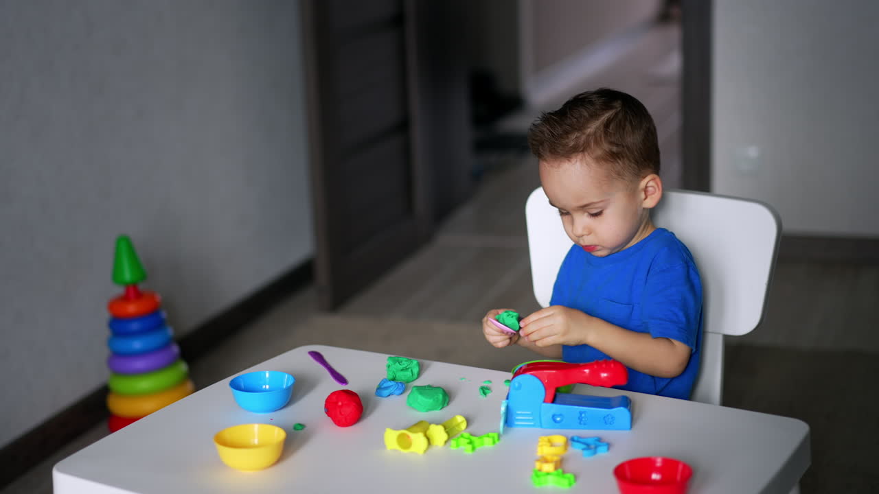 Adorable toddler playing at the desk in his room. Cute child playing with plasticine at home.