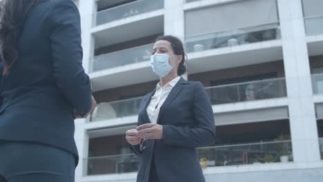 colegas de negocios con máscaras faciales reunidos en el edificio de oficinas, saludándose con golpes en los codos y hablando