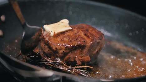 delicious meat steak is fried with butter and rosemarie in a dark pan