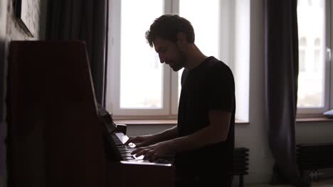 bearded man professionally play the piano at home against window