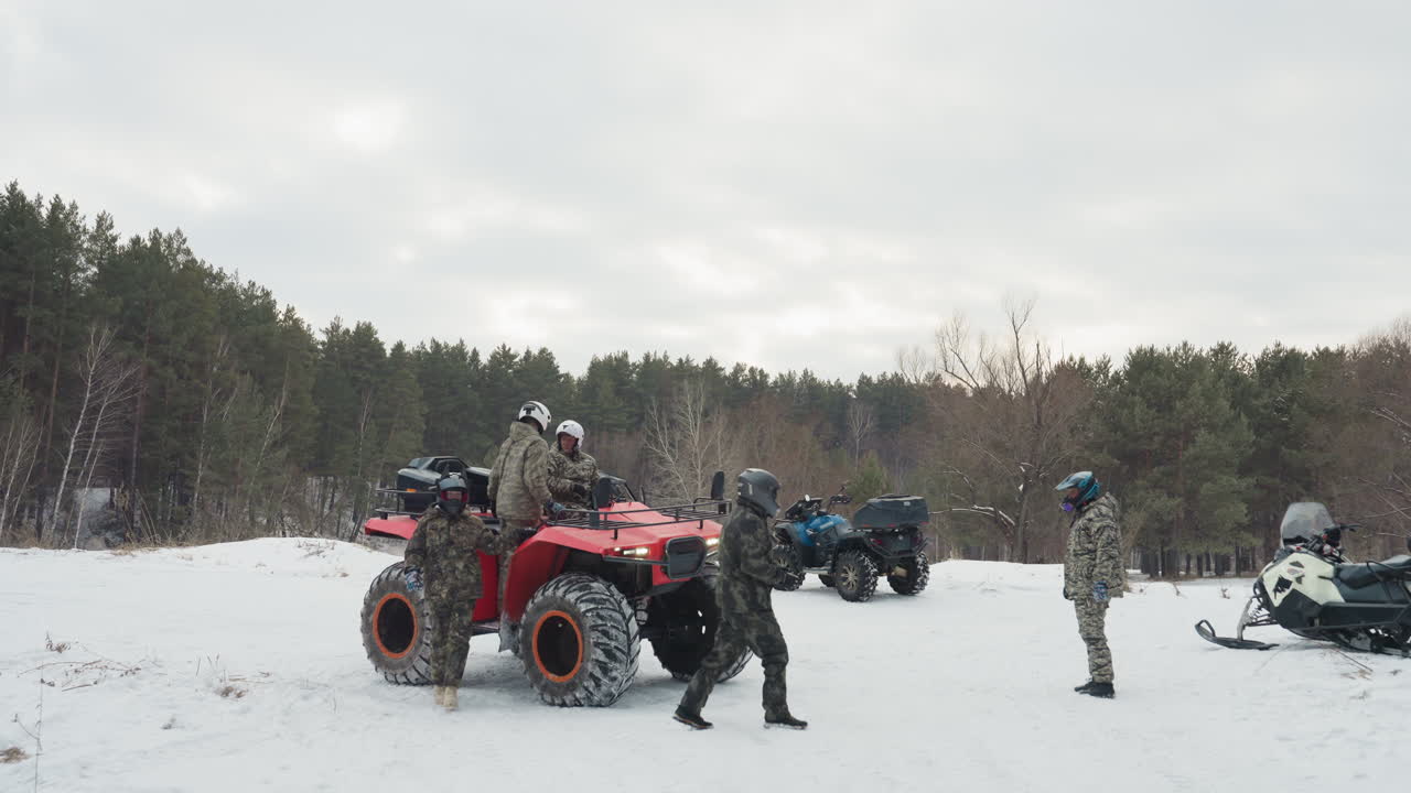 Ritrovo di quad in una foresta innevata con piloti che preparano i loro mezzi, quad rosso in primo piano, il gruppo controlla caschi e attrezzatura, una motoslitta parcheggiata nelle vicinanze, cielo coperto e sfondo di pini, lavoro di squadra e motore.