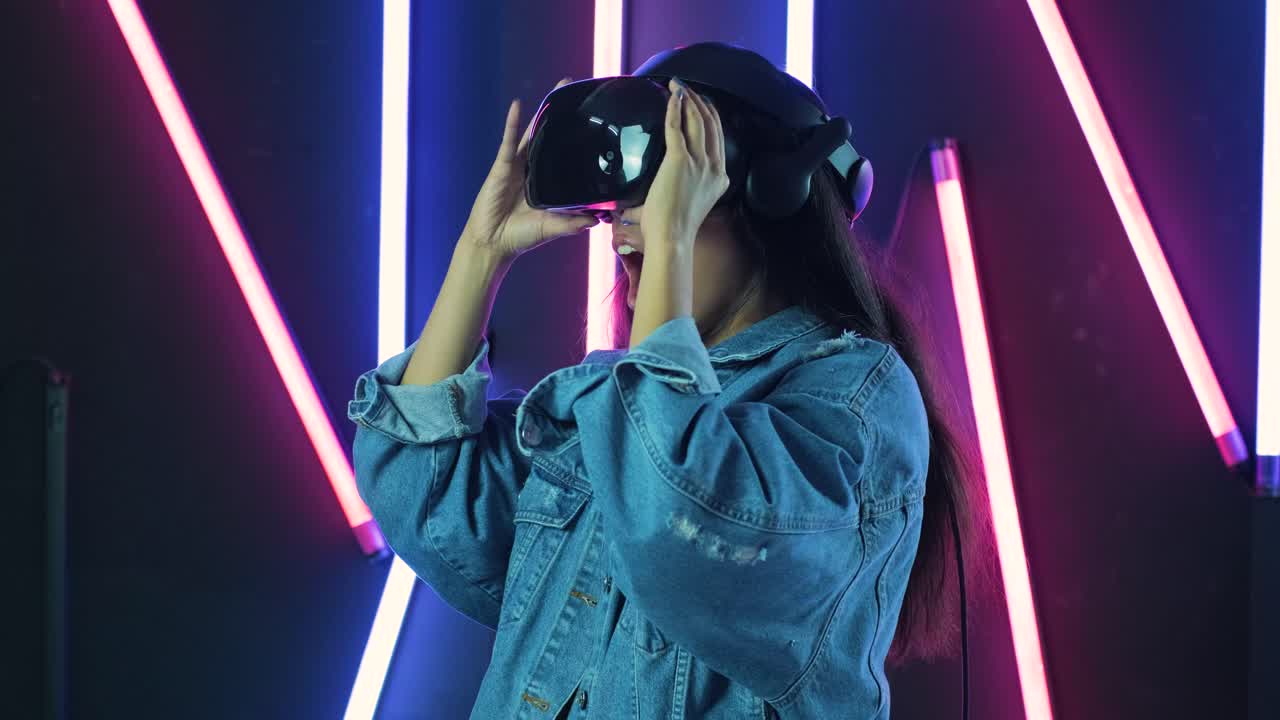 Giovane donna che indossa il visore VR e si meraviglia di quanto sia incredibile nel mondo della realtà virtuale. Casco per la realtà virtuale su sfondo illuminato a colori.