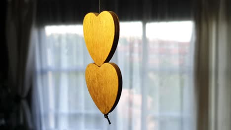 Double-brown-wooden-hearts-on-a-string-of-a-wind-chime-moving-and-turning-as-wind-blows-into-living-room