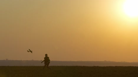 the boy is launching the toy plane into the sky and it is making a loop. outdoor games at sunset. 4k