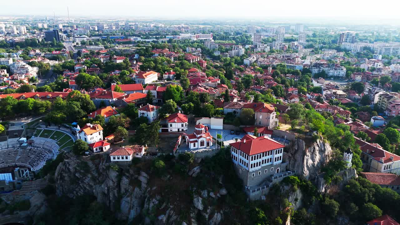 Um drone se afasta e eleva-se da Igreja de São Jorge, revelando toda a beleza de Plovdiv enquanto a cidade se esvai na neblina.