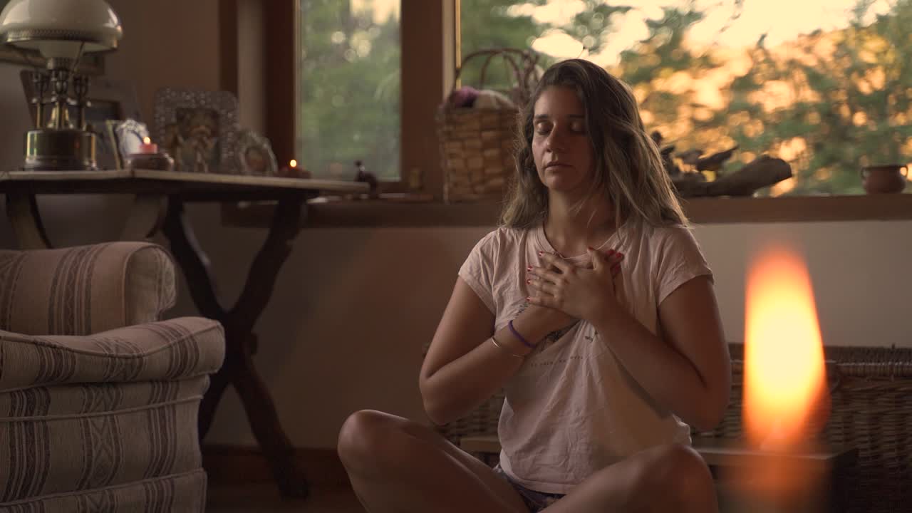 Young female latin meditating sitting on a pillow in casual indoor spiritual studio with big green window with vegetation in a wooden home slow motion 60fps