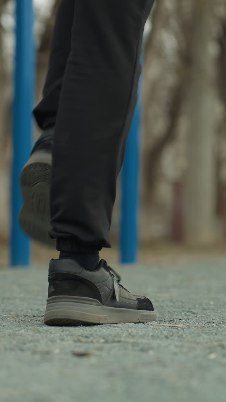 Close-up of a person s legs wearing a black jeans and canvas jogging quickly, with a blurred view of a cars passing from the left across the road and blue iron bars in the background