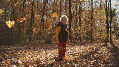 A-little-smiling-curly-boy-watches-the-leaf-drop-while-standing-in-an-autumn-park.-Watch-the-falling-leaves-fall-in-the-sun-in-slow-motion.-High-quality-4k-footage