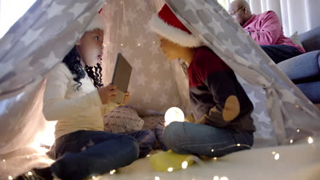 Happy-african-american-brother-and-sister-in-christmas-hats-with-tablet-in-blanket-tent,-slow-motion