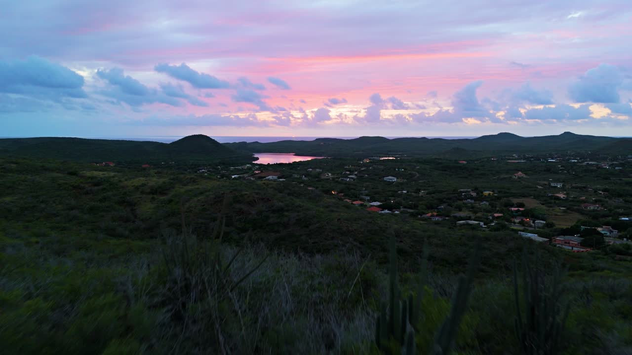 Drone ascend above cactus on hills to reveal Curacao countryside, fire red glow in wispy sunset clouds