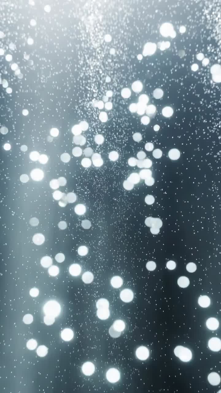 Vertical video: Rising bubbles lifting bokeh in tank, lit by veils on blue-gray panel