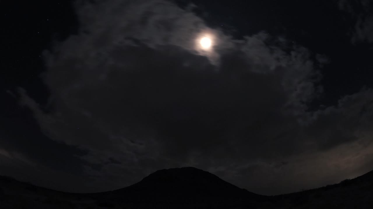 실루엣 산 위의 모하비 사막에서 달과 구름의 야간 저속 촬영