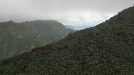 Hiker-with-backpack-descends-mountain-ridge-trail-on-Hawaii,-aerial