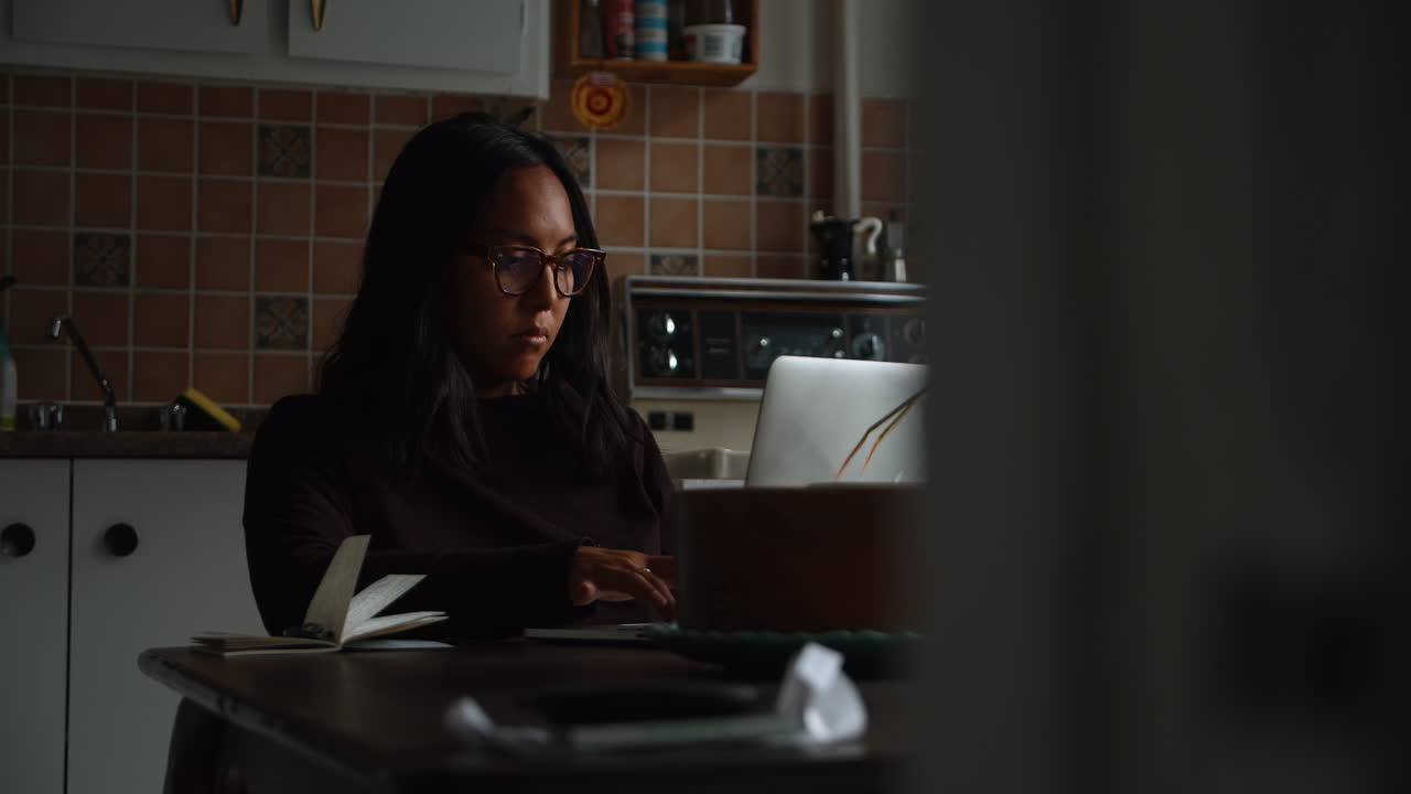 Una donna digita sul suo computer portatile mentre è seduta nella sua postazione home office lavorando nel pomeriggio in sala da pranzo