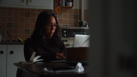 A-woman-types-on-her-notebook-computer-as-she-sits-in-her-home-office-setup-working-in-the-afternoon-in-the-dining-room