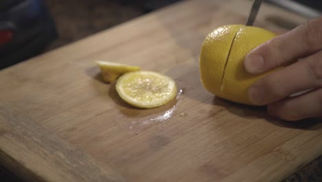 a person hands slowly cutting a fresh lemon on a cutting board - close up shot