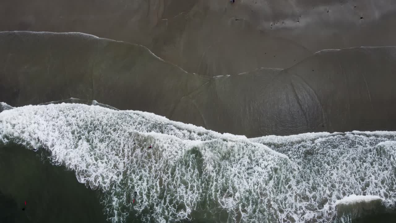 Waves rolling onto the sand on a beach along the coast of Northern California during Summer. The white water hits the sand with force. 4K cinematic drone footage.