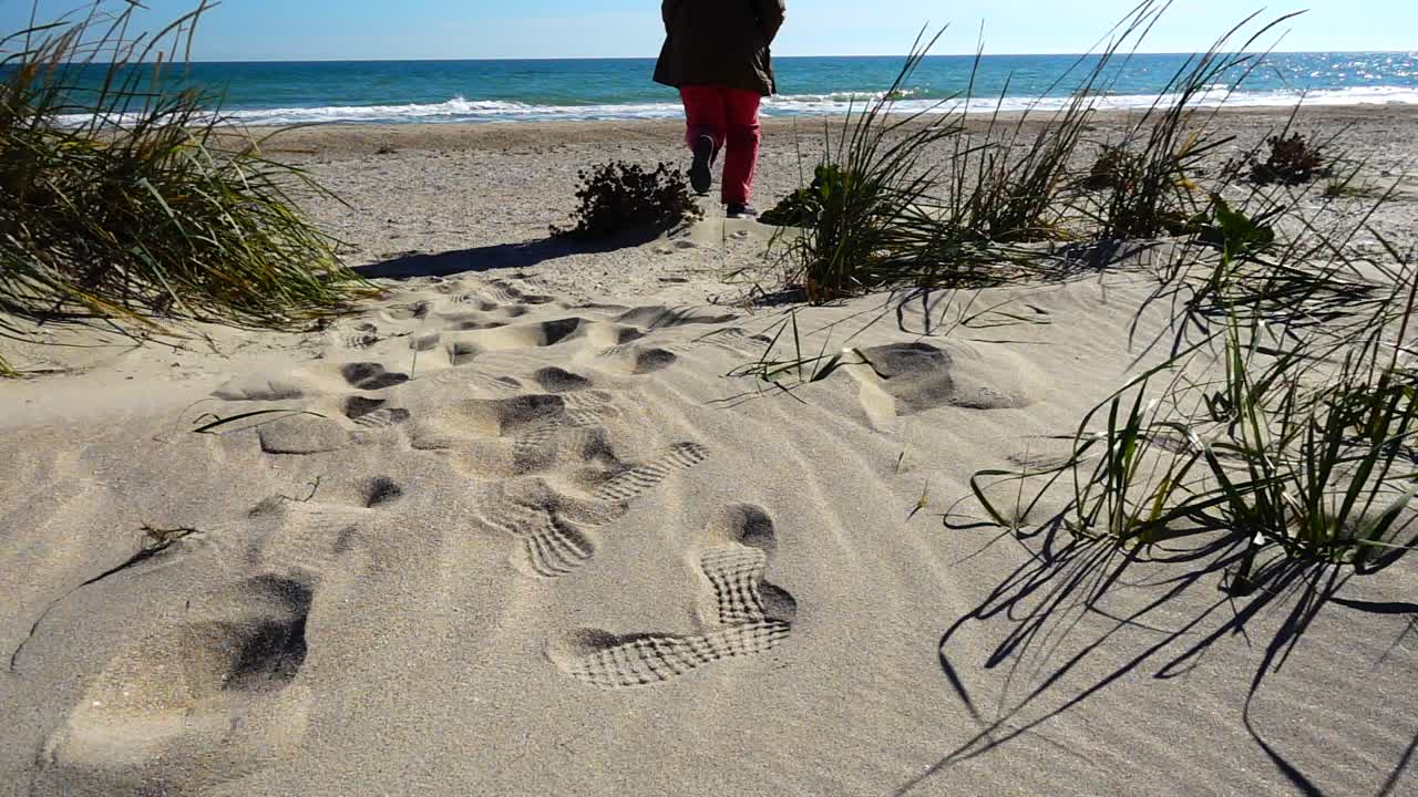 Kvinnen løper på sanddyner til havet. Sakte film.