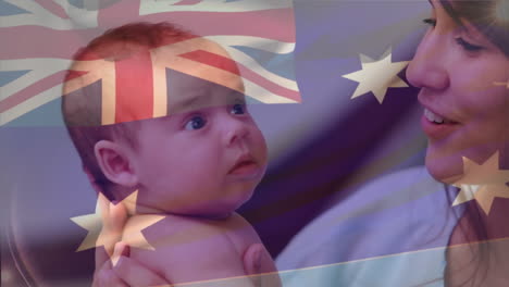 composite video of waving australia flag against happy caucasian mother kissing her infant baby