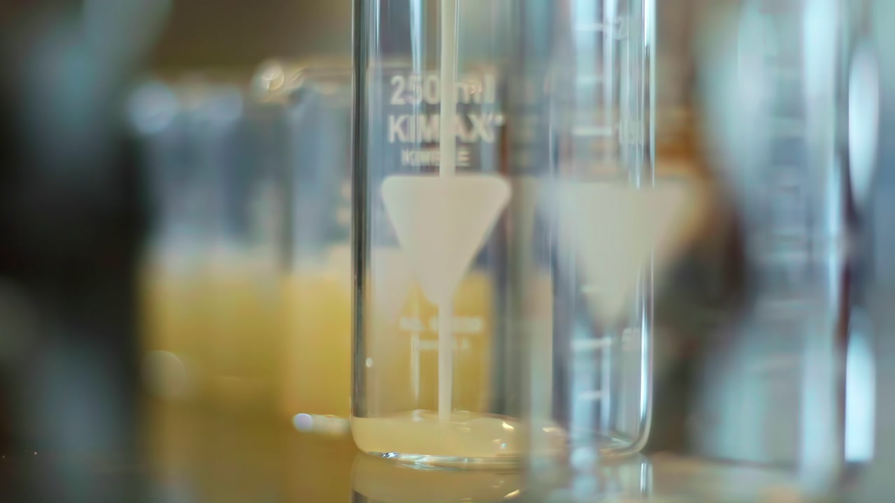 Clear fluid filling small lab beaker, slow controlled pour, clinical background