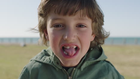 portrait of cute caucasian boy making faces looking at camera happy playful enjoying sunny seaside park